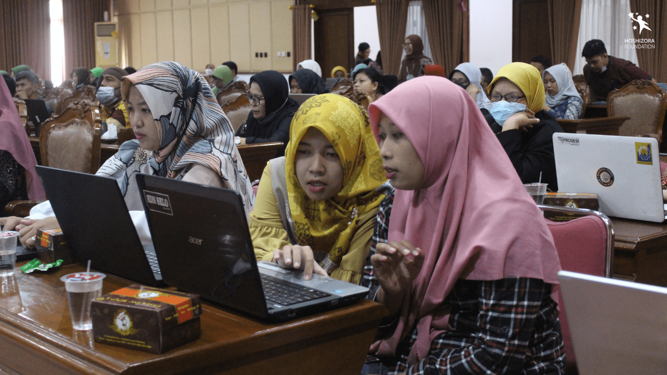 Guru berkerudung kuning (kiri) menunjukkan sesuatu pada layar laptop kepada guru berkurudung pink (kanan) di acara Sepatu Untuk Guru tahun 2022. Hari Guru Sedunia: Pentingnya Mendukung Guru untuk Pendidikan Berkualitas dengan Hoshizora Foundation