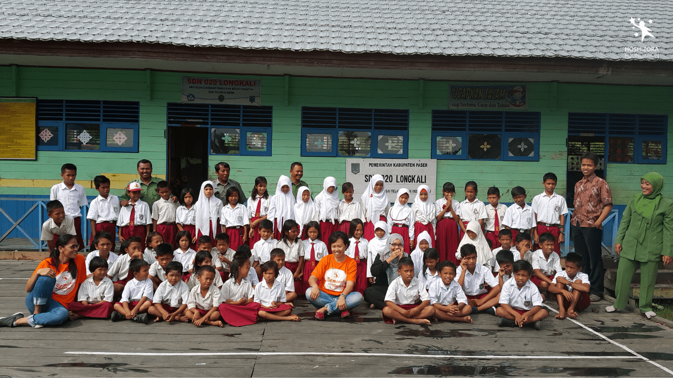 Guru dan murid SDN 20 Longkali, Paser, Kalimantan Timur serta staf Hoshizora Foundation berfoto bersama di depan gedung sekolah. Sejarah Hari Guru Sedunia.