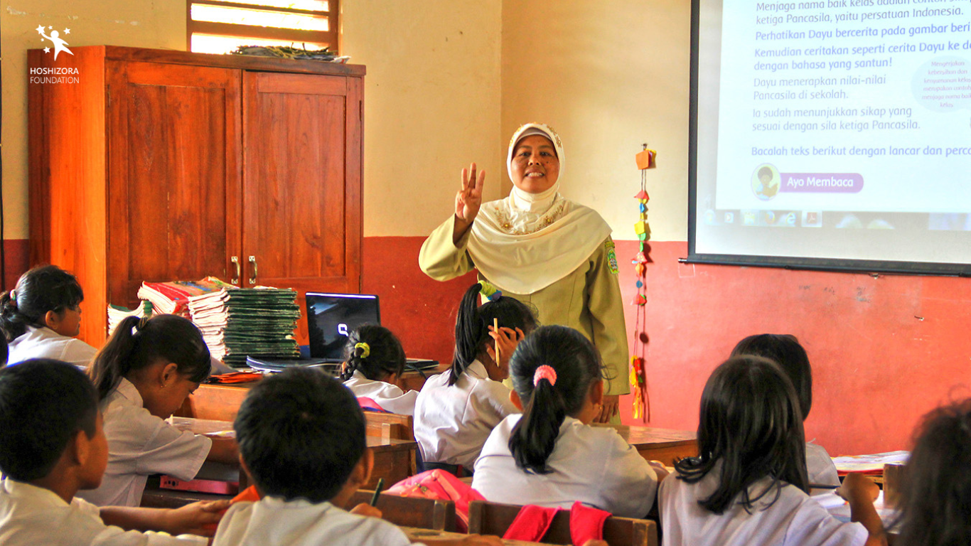 Potret seorang guru perempuan berkerudung putih yang sedang mengajarkan mata pelajaran Pancasila kepada anak didiknya di kelas. Hari Guru Sedunia, Perlukah Dirayakan?